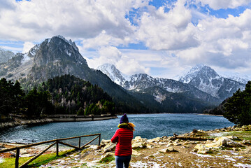 Woman in red coat at Sant Maurici Lake with snowy mountains, in Aigües Tortes National Park, in...