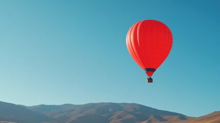 Obraz premium Bright Red Hot Air Balloon Floating in Clear Blue Sky Over Mountain Landscape