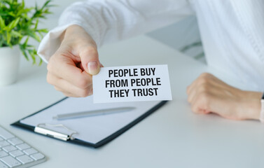 A person is holding a piece of paper that says People Buy From People They Trust. The image conveys the importance of trust in business transactions.