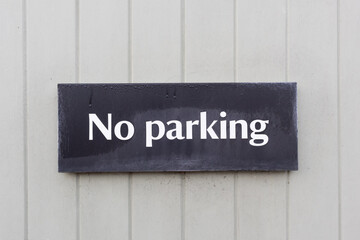 No Parking sign on painted wooden background.  Black sign with white letters.