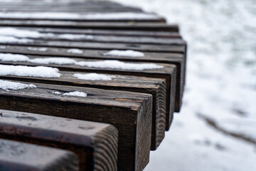 A wooden bench shows remnants of snow while surrounded by a cold, frozen landscape in a winter setting