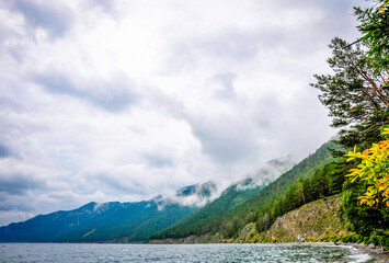 Landscape of blue deep lake in light of sun in daytime, clouds in sky, mountains