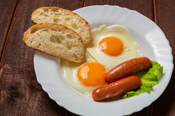 Breakfast fried eggs with sausages fresh croutons, on a brown wooden table