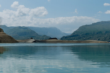 Landscape of blue deep lake in light of sun in daytime, clouds in sky, mountains