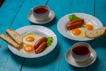 Breakfast for two fried eggs with sausages fresh toast and tea in cups on a blue wooden table