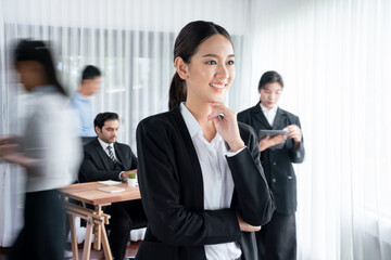 Portrait of happy young asian businesswoman looking at camera with motion blur background of business people movement in dynamic business meeting. Habiliment