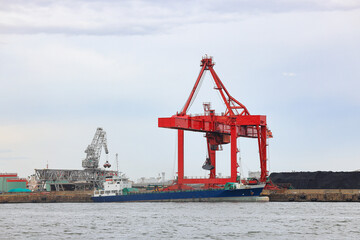 Large crane works on large coal stockpile and container crane at Industrial port for cargo container ship. Cargo transportation and activity at modern shipping container terminal.
