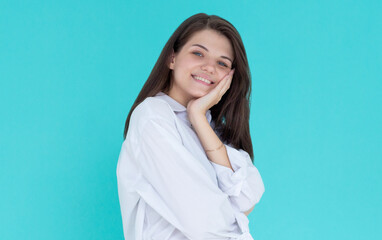 Portrait of young stylish girl smiling with hand on cheek looking at camera. Copy space. Isolated on blue background