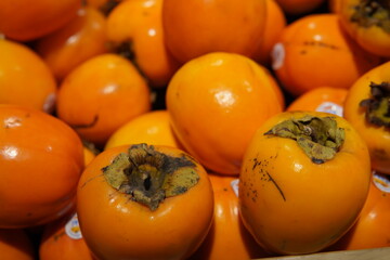 Persimmons are neatly arranged on a market shelf. Bright, smooth, shiny and orange. Suitable for themes related to seasonal products, healthy eating or food retail.