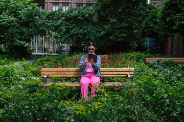 Young woman using tablet and making video call while sitting on bench in city park