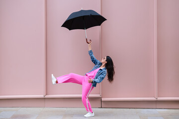 Young stylish woman balancing with umbrella on pink wall background