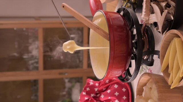 Cozy Swiss fondue setup with melted cheese, bread, pickles, and wine on a rustic table. advertising, social media campaigns, or food-related promotions. High quality 4k footage