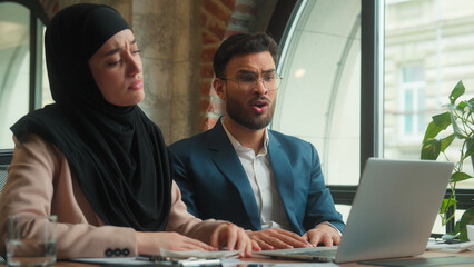Multiethnic business colleagues Arabian Indian man Muslim woman in hijab looking laptop expect wish hope businesswoman businessman upset displeased bad result problem loss failure bankruptcy at office