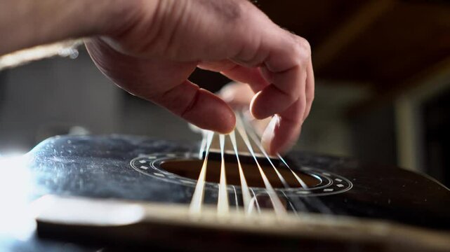 man plays acoustic guitar and touches the strings with his fingers close-up, musician plays music on black guitar