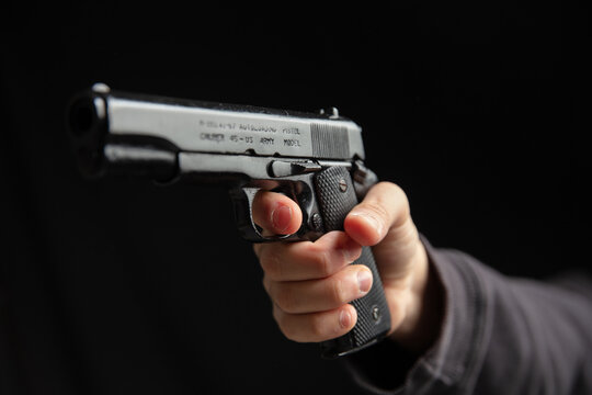 Hand holding a gun closeup, armed man on dark background. Danger and crime