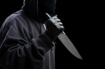 Criminal holding a knife, hooded man holding a weapon in gloved hand, armed attack concept.