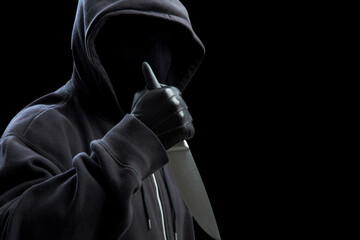 Criminal holding a knife, hooded man holding a weapon in gloved hand, armed attack concept.