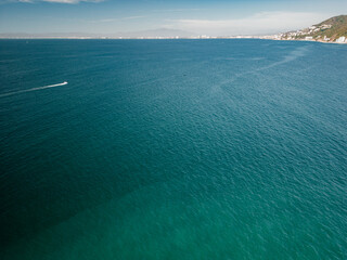 Wide expansive views of turquoise ocean below and Puerto Vallarta in the distance and boat driving.