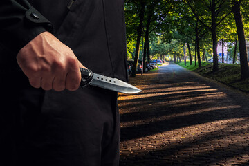 Criminal holding a knife closeup view, city park street background
