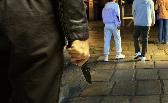 Criminal holding a knife closeup view, dark city street background