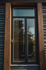 Fototapeta premium Modern black and wood door with glass panels, reflecting greenery and a seating area outside.