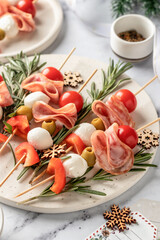 Snack skewers with mozzarella, ham, olives, peppers, tomatoes. Festive canapes or antipasti on white tray for new year table