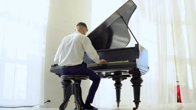 young guy in white shirt plays classical music on the piano, musician performs melody on musical instrument