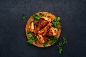 Baked chicken legs or drumsticks in spices on wooden serving board, black background, top view