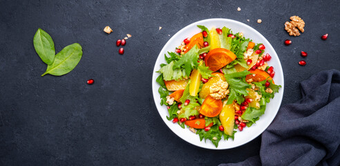 Winter vegan  persimmon salad with pomegranate, walnuts, oranges and lettuce, black background, top view