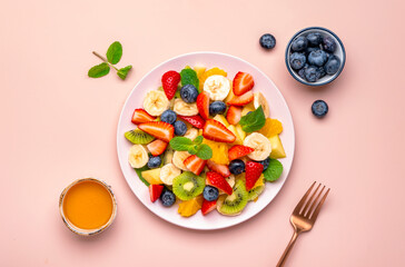 Yummy vegan fruit salad with strawberries, blueberries, banana, kiwi, orange and mint, pink background, top view