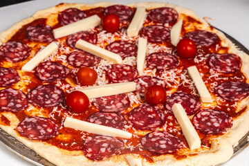 Pizza is prepared for baking. Raw pepperoni pizza with sausage, mozzarella cheese, cherry tomatoes and basil on a baking wheel