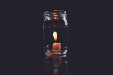 A glass jar containing a candle that burns in the dark