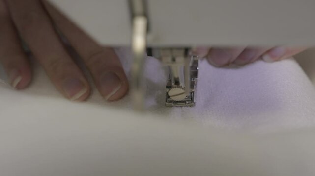 This video shows a close up view of stitcher's hands passing white fabric through a sewing machine.