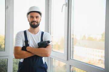 Workman in overalls installing or adjusting plastic windows in the living room at home