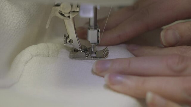 This close up, side view video shows skilled stitcher hands sewing a seam of white upholstery fabric on a sewing machine. 