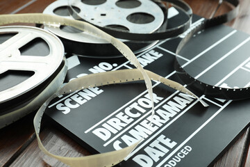 Movie clapper and film reels on wooden table, closeup