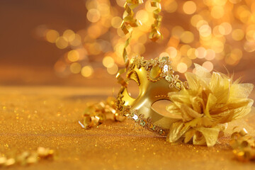Beautiful carnival mask on golden shiny surface, closeup. Space for text