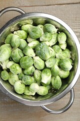 Fresh Brussels sprouts in metal colander on wooden table, top view