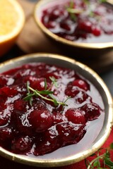 Tasty cranberry sauce in bowls and thyme on table, closeup
