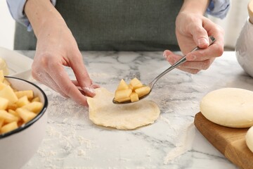 Woman making pirozhki (stuffed pastry pies) with apples at white marble table, closeup