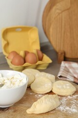 Making pirozhki (stuffed pastry pies). Pieces of dough with cottage cheese on table, closeup