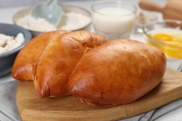 Delicious pirozhki (stuffed pastry pies) and ingredients on white wooden table, closeup
