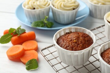 Delicious carrot muffins and fresh vegetable on white wooden table, closeup