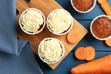 Delicious carrot muffins and fresh vegetables on blue wooden table, flat lay