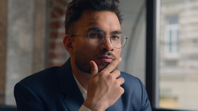 Pensive guy Arabian Indian business man thinking looking at camera close up male thoughtful puzzled businessman office think question idea solution problem search choose decide consider ponder serious