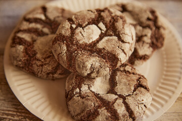 A full paper plate with chocolate cookies with cracks on a wooden table, macro shot, homely atmosphere, sweet baking.