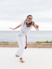 Woman in white practicing capoeira outdoors, smiling, by the seaside with ocean view