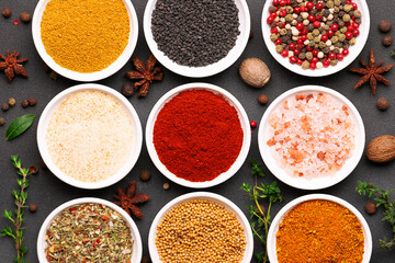 Bright set of aromatic organic spices and herbs such as smoked paprica, peppercorn, thyme, bay leaf, curry, dry garlic and others on black stone background top view.