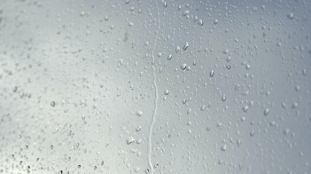 Experience the beauty of rainy weather as raindrops cascade down a window in stunning close-up. Perfect for conveying emotions of calmness, nostalgia, and the soothing sound of rain