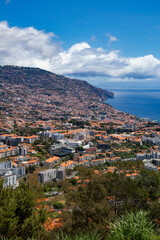 Panoramic view of Funchal, the capital of Madeira Island, showing the city sprawled along the hillside with the Atlantic Ocean in the background on a sunny summer day.